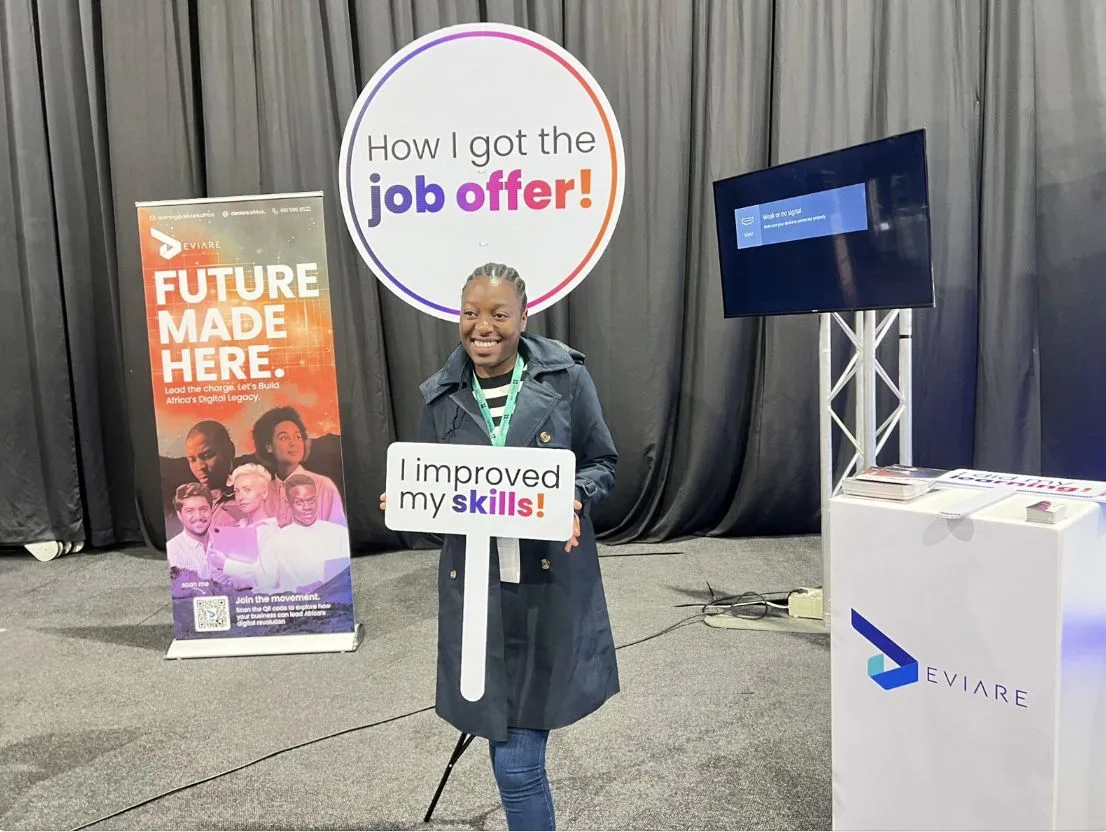 A young professional at a Deviare careers stand holding an \u201cI improved my skills!\u201d sign